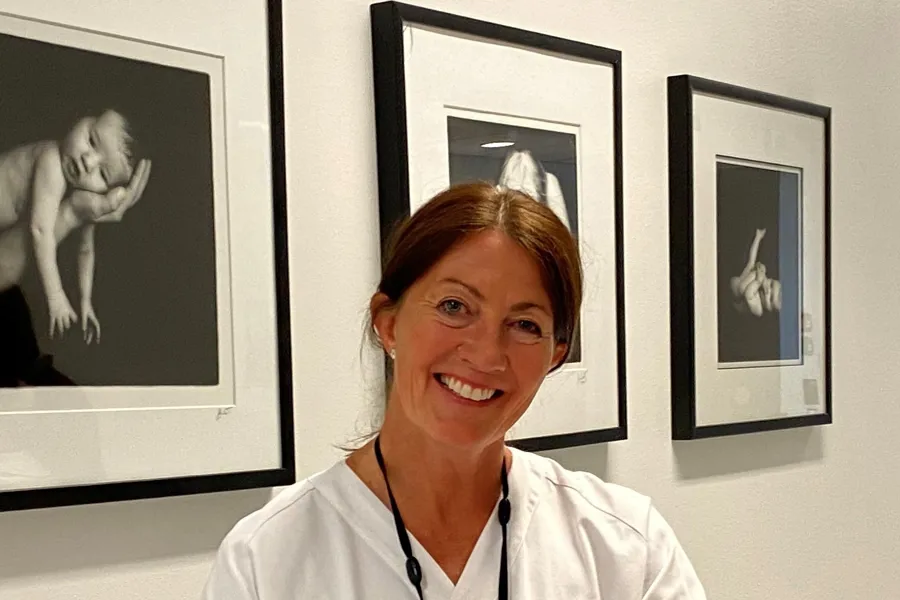 En person som smiler foran en vegg med bilder