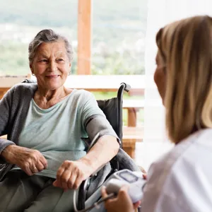 Illustrasjon: En eldre dame i rullestol prater med en sykepleier