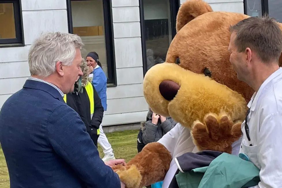 En gruppe mennesker som står ved siden av en person i et bjørneklær