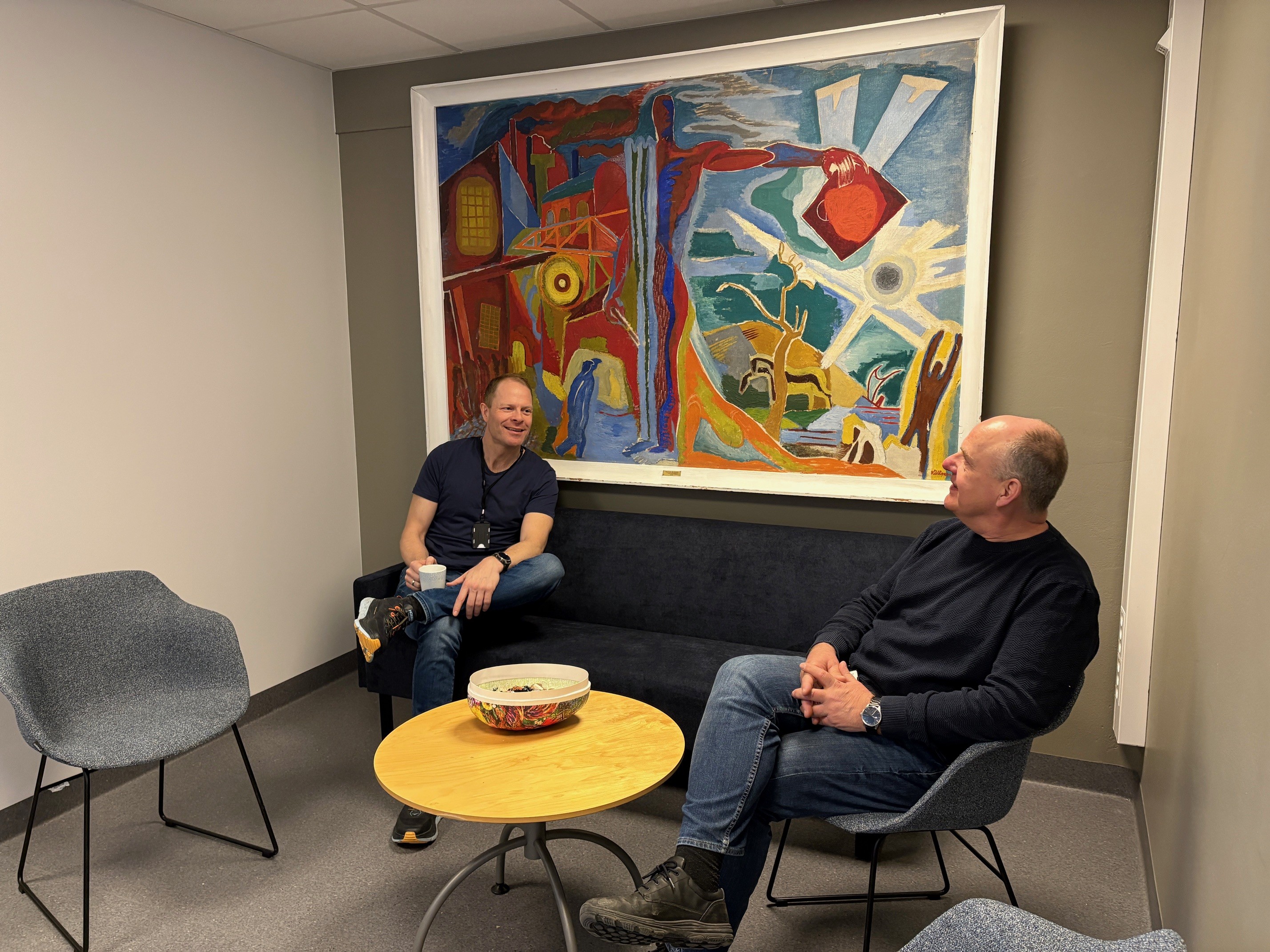 Menn som sitter i stoler foran et maleri