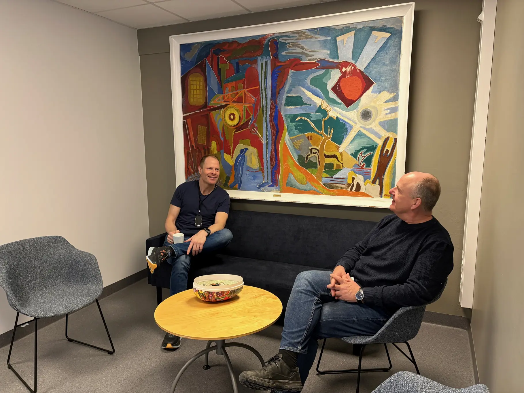 Menn som sitter i stoler foran et maleri