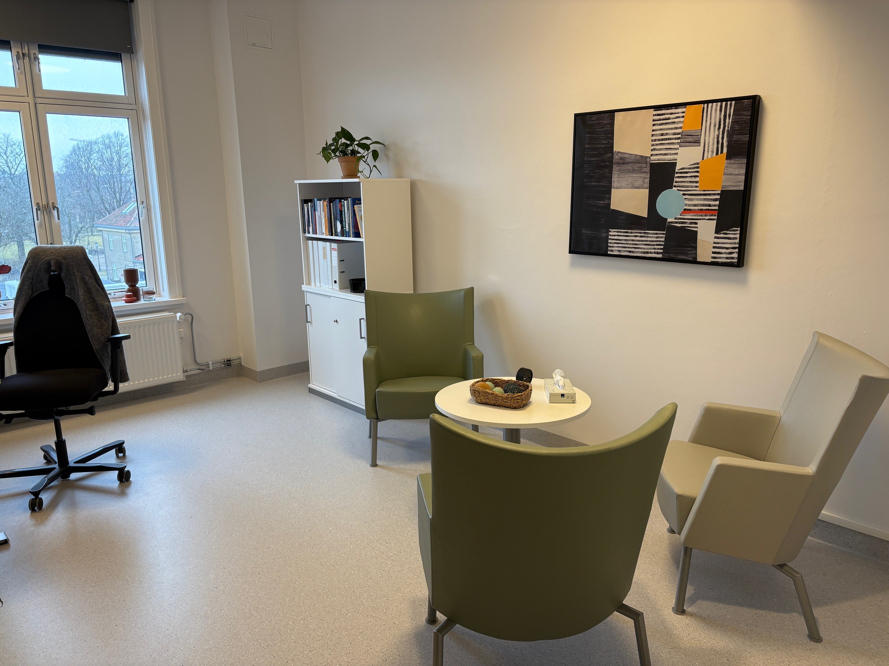 Et rom med grønne stoler og et bord, med et bilde på veggen