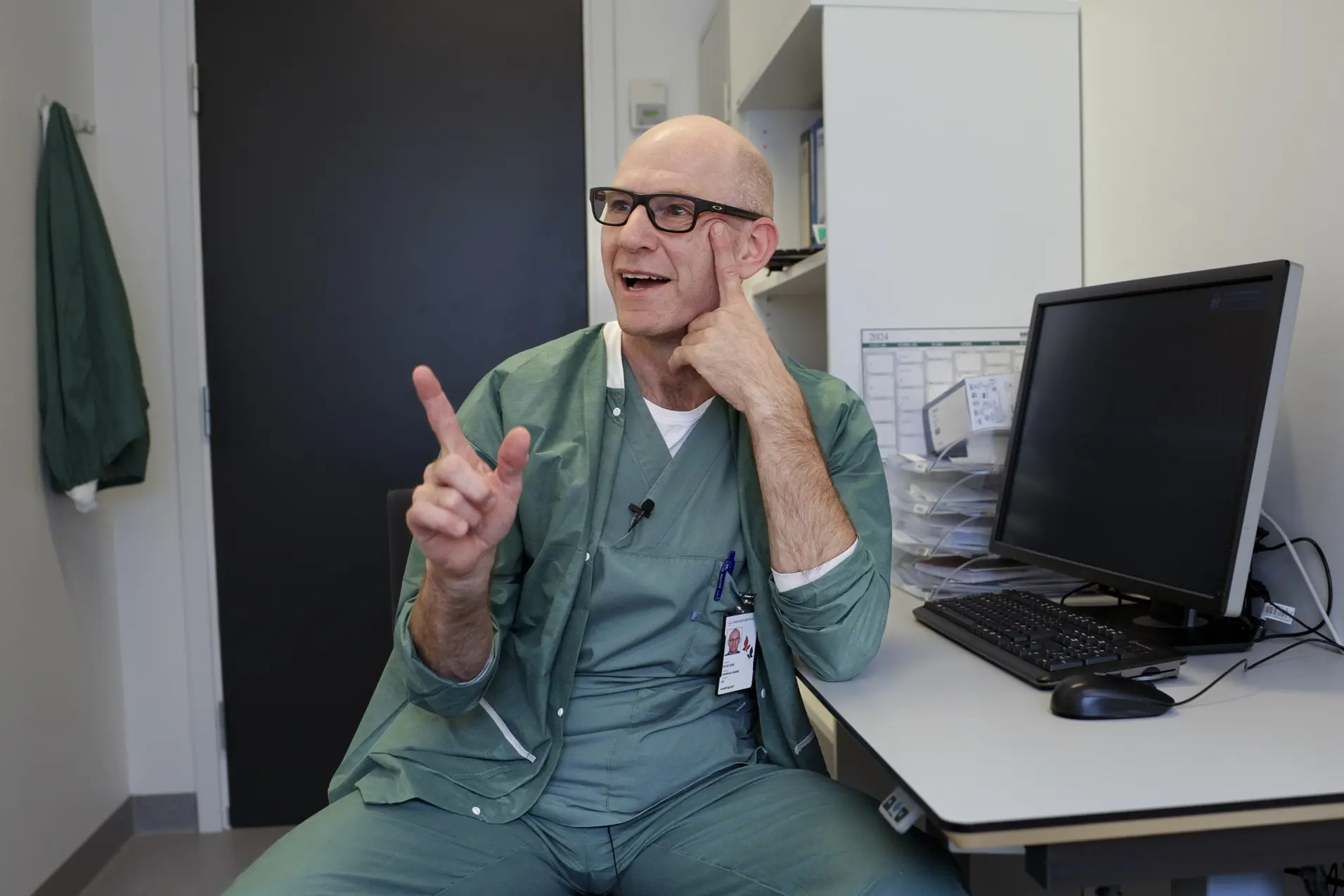 En mann som sitter ved et skrivebord med hånden opp