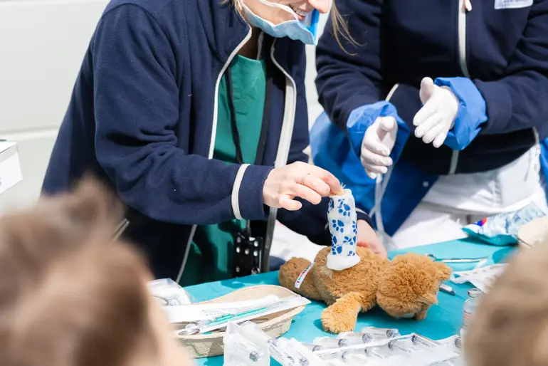 En person i arbeidsklær og maske som holder en teddybjørn