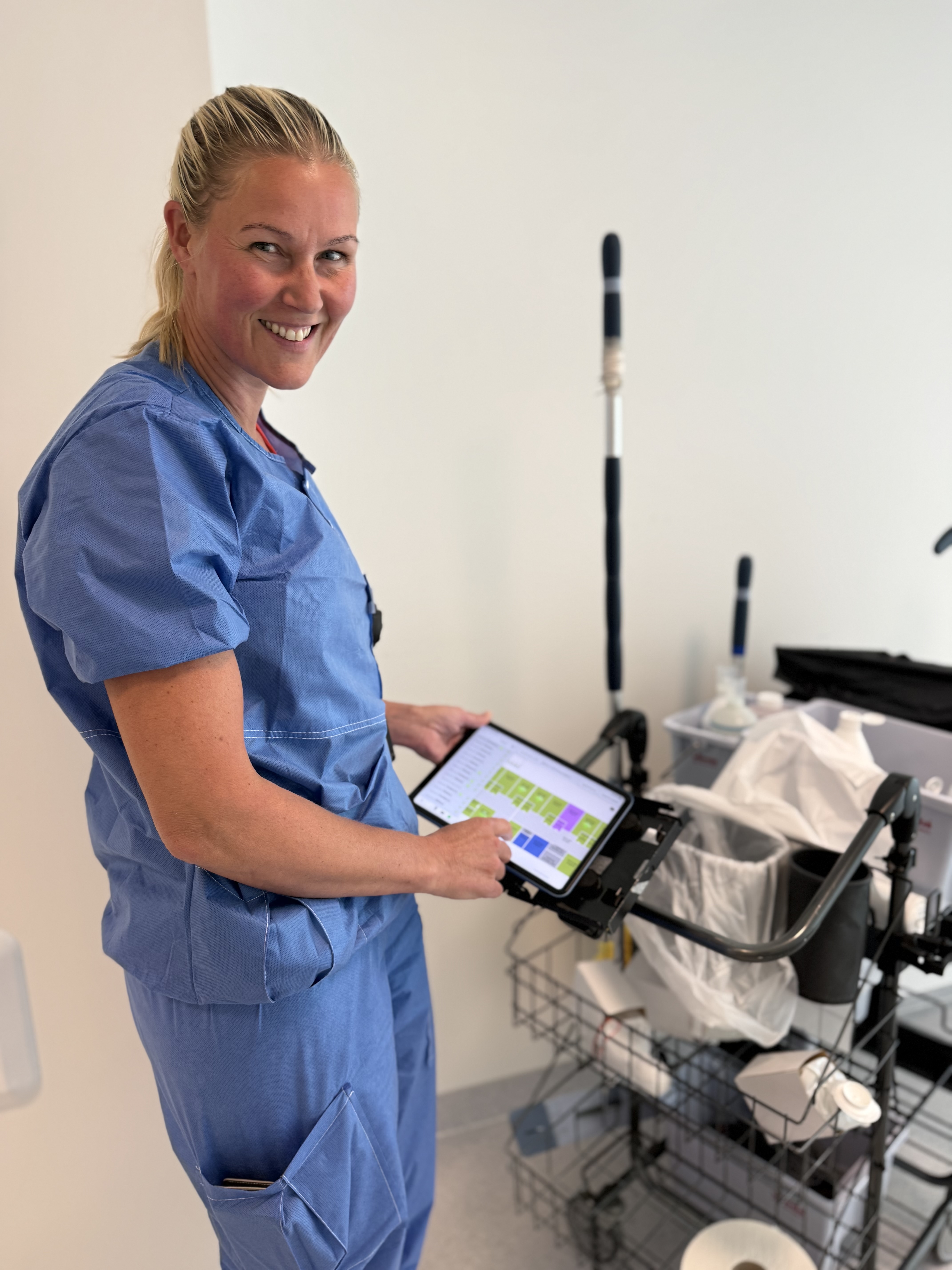 Marianne Holme viser fram renholdstralle og ipad med arbeidsoppgavene på