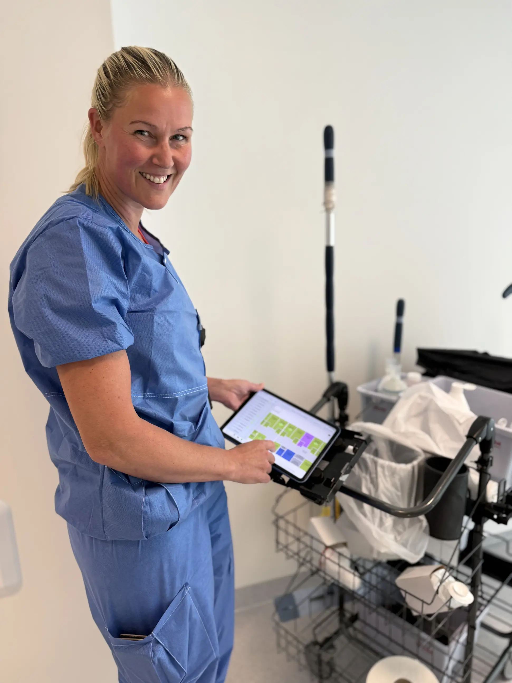 Marianne Holme viser fram renholdstralle og ipad med arbeidsoppgavene på