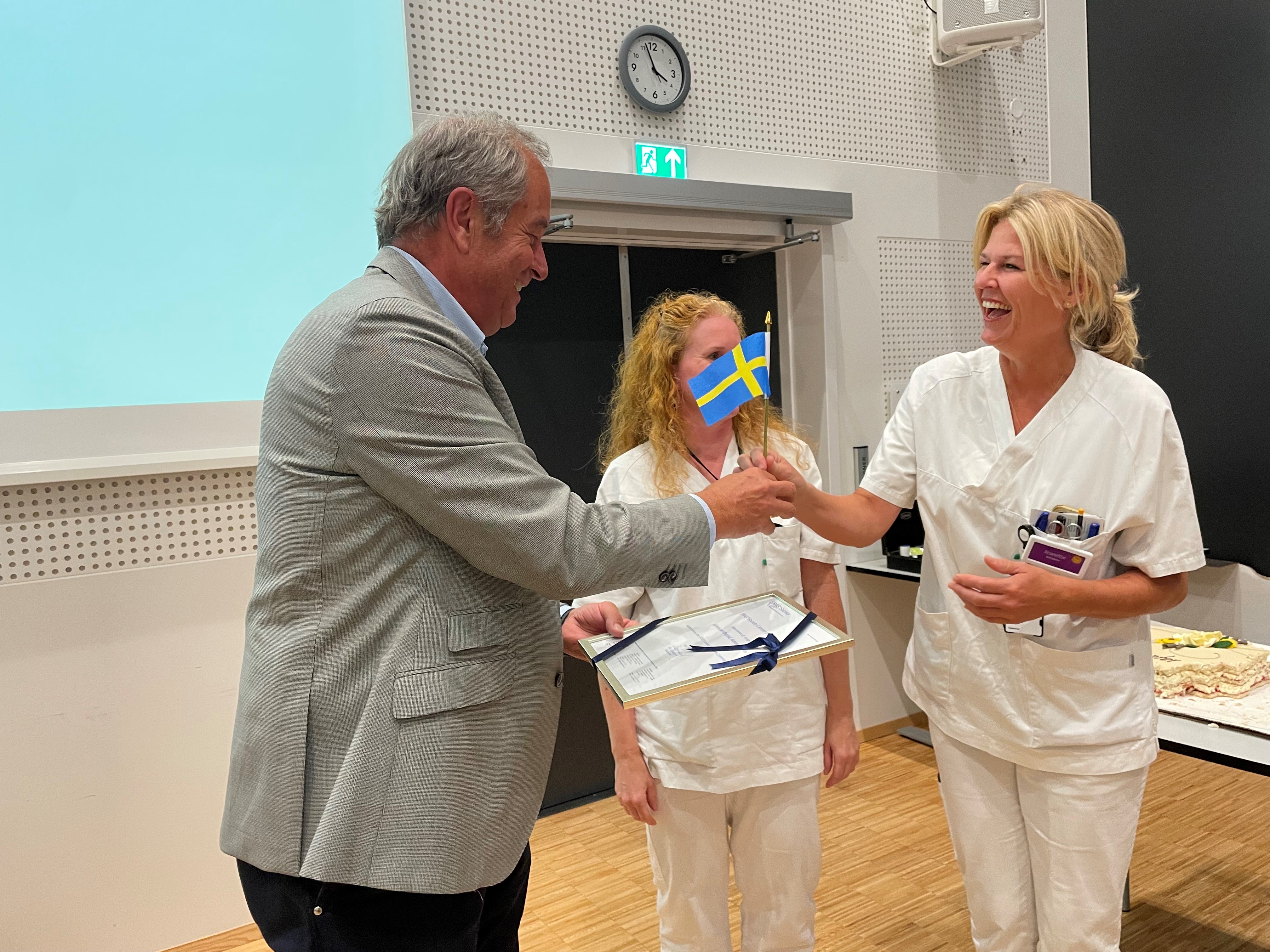 En sykepleier får et svensk flagg og et diplom av  professor Olle Ljungqvist