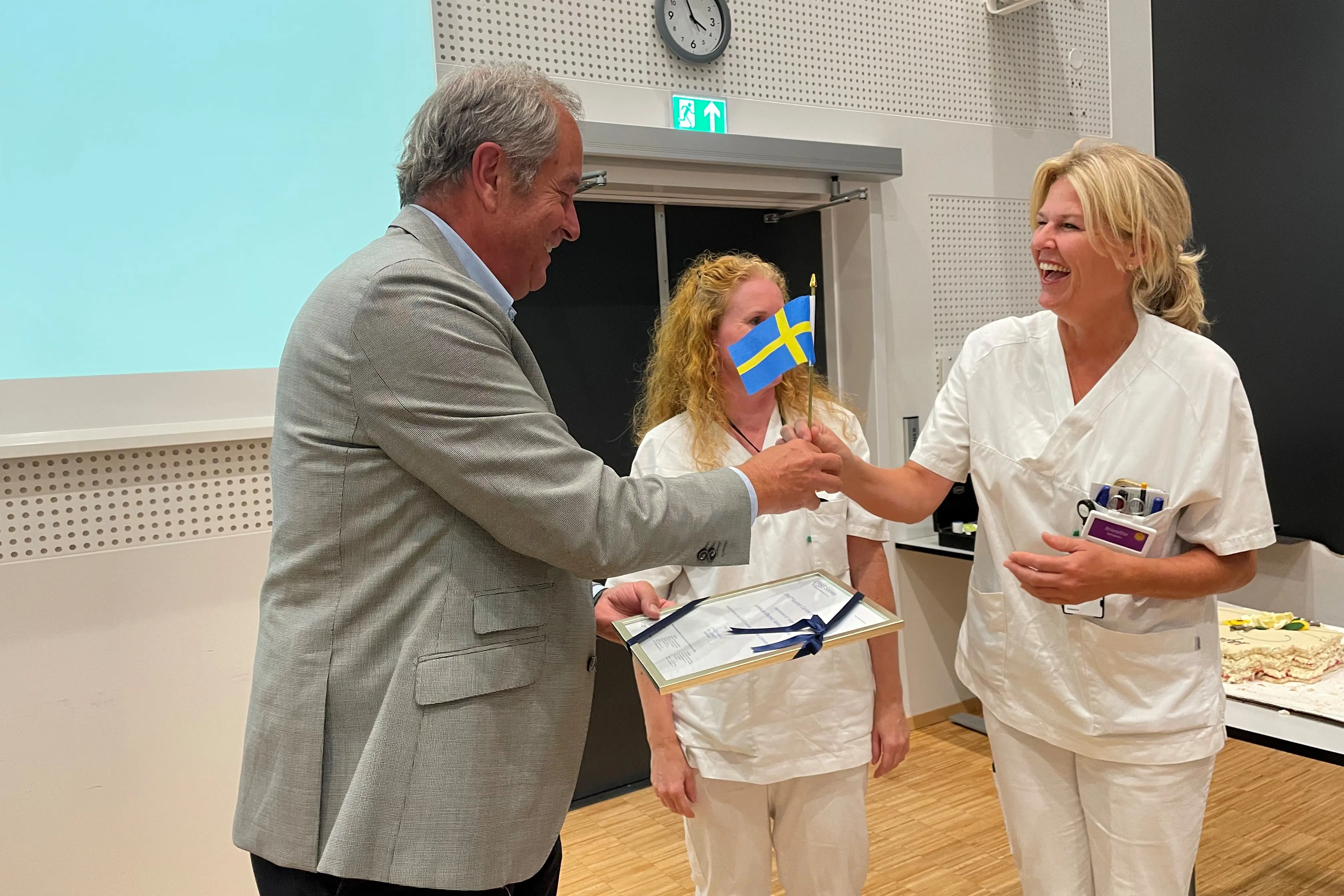 En sykepleier får et svensk flagg og et diplom av professor Olle Ljungqvist