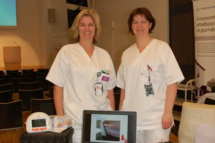 Et par kvinner i hvite frakker som står ved siden av en bærbar datamaskin