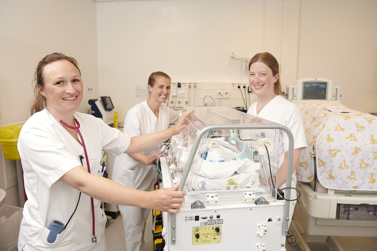 Tre medarbeidere på nyfødtintensiv står rundt en kuvøse