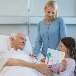En kvinne og en jente står ved sykehussengen til en eldre mann